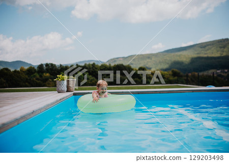Little girl playing in shallow water in pool, using swim ring. 129203498