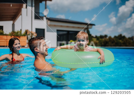 Family swimming with toddler in backyard pool 129203505