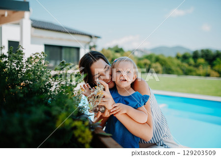 Mom and little toddler taking care of plants in garden, spraying them with water. 129203509