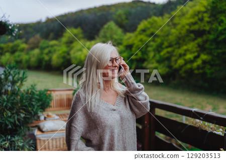 Senior woman standing terrace making phone call. Senior woman standing terrace making phone call. 129203513