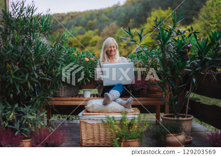 Older woman working from homeoffice, sitting on terrace with laptop. 129203569