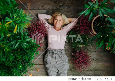 Senior woman lying on terrace with autumn plants. 129203595
