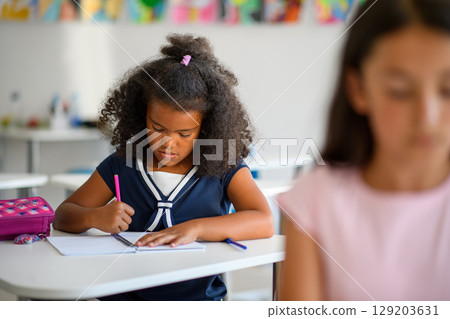 Focused schoolgirl writing notes in classroom. 129203631