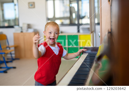Boy with Down syndrome playing piano at school. Boy with Down syndrome playing piano at school. 129203642