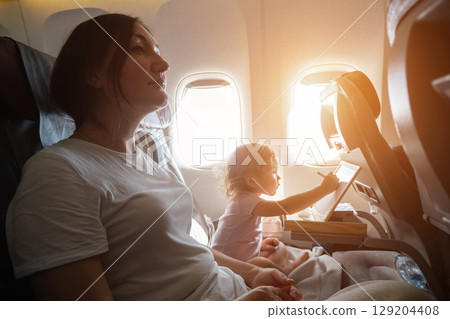 Mother and daughter relaxing on airplane during flight 129204408