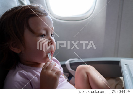 Toddler girl eating yogurt on airplane near window 129204409