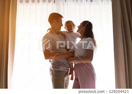 Happy family embracing near window in morning light Happy family embracing near window in morning light 129204421