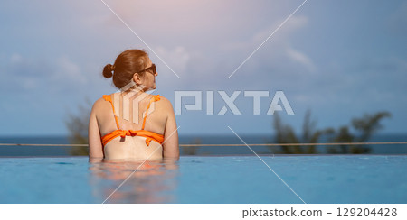 Tourist relaxing in infinity pool enjoying ocean view Tourist relaxing in infinity pool enjoying ocean view 129204428