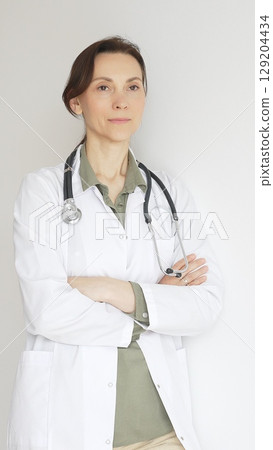 Female medical professional in white lab coat, stethoscope draped, standing with crossed arms and displaying confident, authoritative healthcare demeanor. Medicine and health care 129204434
