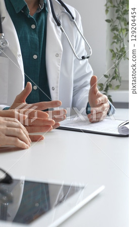 Doctor man wearing medical coat over green shirt, and stethoscope is gesturing with hands over white table while explaining diagnosis to patient. Medicine and health care concept 129204454