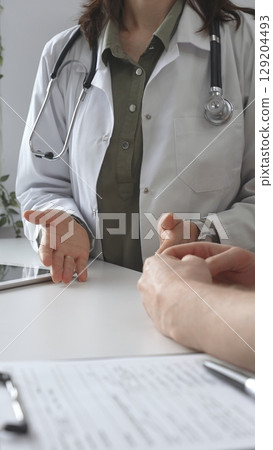 Doctor woman in medical coat is explaining diagnosis to male patient during a medical consultation in a medical office, gesturing with hands, vertical close up view. Medicine and health care 129204493