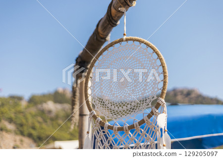 A detailed dreamcatcher is suspended from a wooden pole, surrounded by lush greenery and a bright blue sky. The intricate design captures the sunlight, creating a serene atmosphere A detailed dreamcatcher is suspended from a wooden pole, surrounded by lush greenery and a bright blue sky. The intricate design captures the sunlight, creating a serene atmosphere 129205097