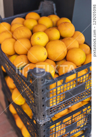 Vibrant oranges fill black crates in a market, showcasing their bright color under sunlight, inviting shoppers to enjoy the fresh fruit Vibrant oranges fill black crates in a market, showcasing their bright color under sunlight, inviting shoppers to enjoy the fresh fruit 129205098