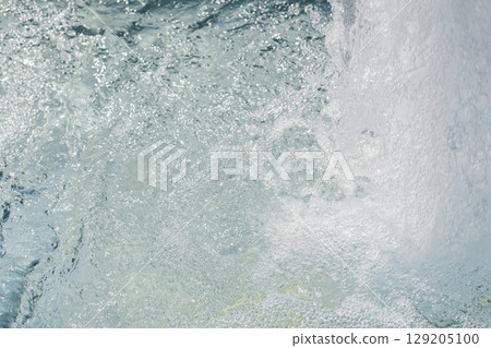 Bubbles rise through crystal clear water from a natural spring, creating a lively atmosphere in a tranquil environment illuminated by bright daylight 129205100