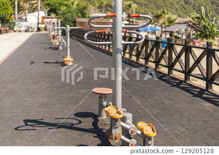 Set beside a scenic beach, an outdoor fitness area features various exercise machines designed for public use, inviting people to enjoy fitness while enjoying nature 129205128