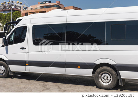 A large white van is parked on a sunny day, displaying a sleek design and tinted windows, surrounded by contemporary architecture in an urban area A large white van is parked on a sunny day, displaying a sleek design and tinted windows, surrounded by contemporary architecture in an urban area 129205195