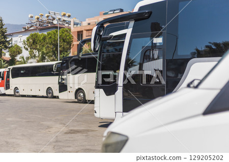 Numerous buses are parked in a transport hub under clear blue skies. The vehicles vary in size and color, showcasing an organized parking area bustling with activity Numerous buses are parked in a transport hub under clear blue skies. The vehicles vary in size and color, showcasing an organized parking area bustling with activity 129205202