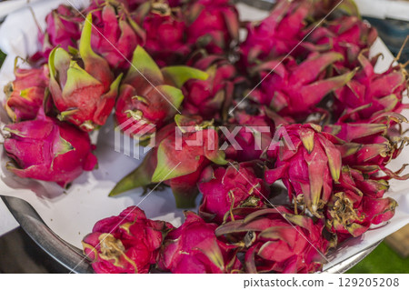 Brightly colored dragon fruit fills a metal tray, showcasing its vivid pink skin and green leaves. These fruits are displayed at a local market in the morning, ready for sale Brightly colored dragon fruit fills a metal tray, showcasing its vivid pink skin and green leaves. These fruits are displayed at a local market in the morning, ready for sale 129205208