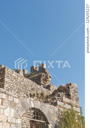Visitors can admire the weathered stone ruins that tell stories of a bygone era. The structure features remnants of intricate architecture against a vibrant blue sky 129205237