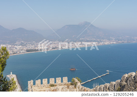 A stunning panorama reveals the azure sea stretching towards the horizon with city buildings dotting the coastline. A historic castle sits atop a ridge, framing the vista A stunning panorama reveals the azure sea stretching towards the horizon with city buildings dotting the coastline. A historic castle sits atop a ridge, framing the vista 129205246