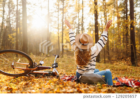 Relax in forest Woman sits on blanket, drinks from thermos, enjoys autumn atmosphere in sunny forest 129205657