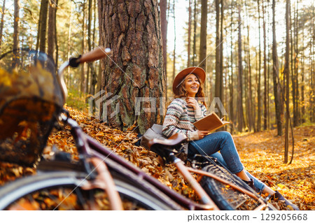 Beautiful young woman sitting on a fallen autumn leaves in a park, reading a book. Beautiful young woman sitting on a fallen autumn leaves in a park, reading a book. 129205668