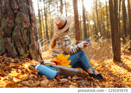 Cute young woman drinks hot drink from thermos and enjoys nature. Autumn landscape. relax concept. 129205670