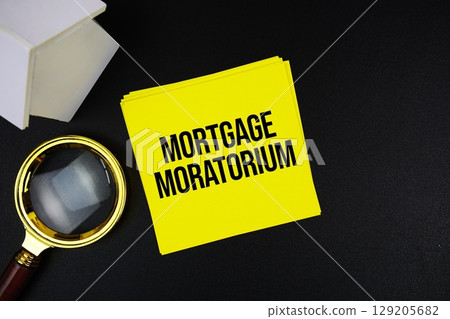 Mortgage Moratorium text message with white house model and magnifying glass top view on black background 129205682