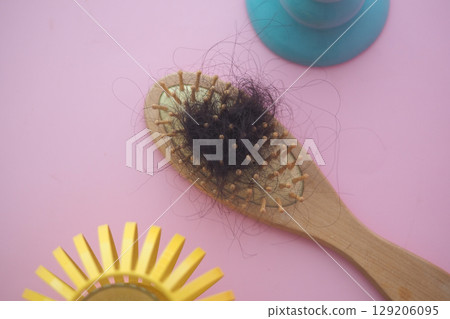A wooden hairbrush with loose hair on a pink background . 129206095