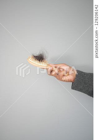 Hairbrush with hair on hand, grey backdrop, hair loss concept Hairbrush with hair on hand, grey backdrop, hair loss concept 129206142