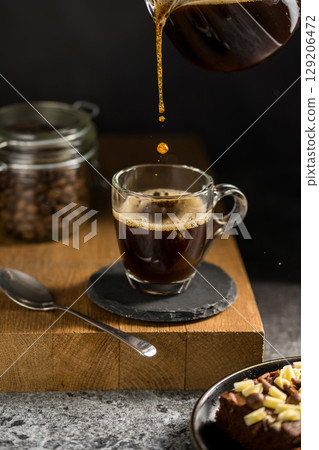 Pouring black coffee in a glass cup, energy coffee drink Pouring black coffee in a glass cup, energy coffee drink 129206472