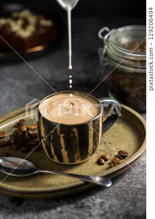 Pouring milk in a cup of coffee, hot coffee with milk 129206494