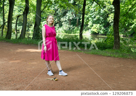 Young woman strolls through a summer park with her agama lizard on a delicate leash Young woman strolls through a summer park with her agama lizard on a delicate leash 129206873