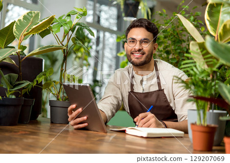 Young male shop assistant making notes while working in the flower shop 129207069