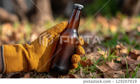 Gloved hand holding a brown beer bottle in an autumn setting 129207819
