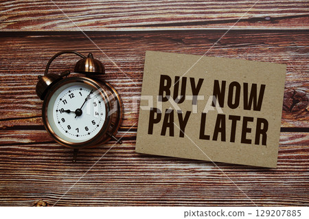 Buy Now Pay Later text with alarm clock on wooden background 129207885
