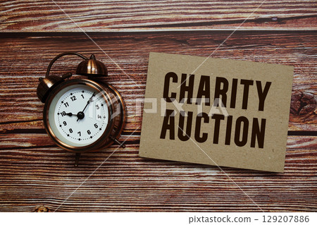 Charity Auction text with alarm clock on wooden background Charity Auction text with alarm clock on wooden background 129207886