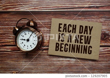 Each day is a new beginning text with alarm clock on wooden background 129207905