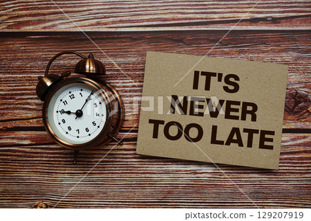 It's Never Too Late text with alarm clock on wooden background 129207919