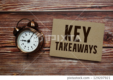 Key Takeaways text with alarm clock on wooden background 129207921