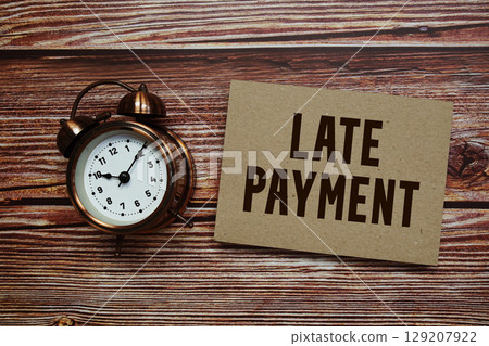 Late Payment text with alarm clock on wooden background 129207922
