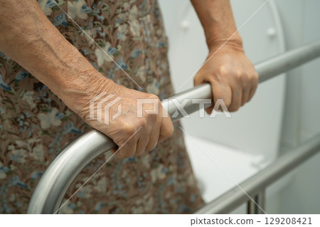Asian elderly woman patient use toilet support rail in bathroom. 129208421