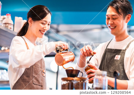 A staff member brewing coffee with a drip kettle and another staff member grounding it 129208564