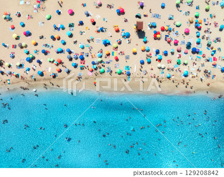 Aerial view of colorful umbrellas on sandy beach, swimming people 129208842