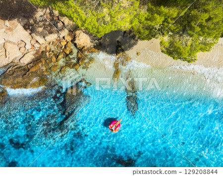 Aerial view of woman on pink inflatable ring in blue sea 129208844