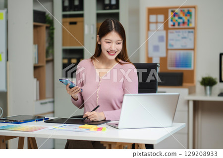 Female coder or developer working using a computer display and smartphone in problem solving at workplace. 129208933