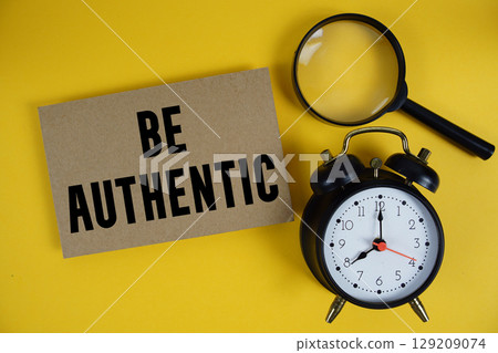 Be Authentic text written on paper with magnifying glass and alarm clock on yellow background 129209074