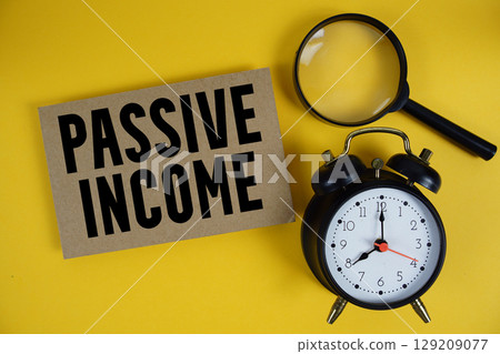 Passive Income text written on paper with magnifying glass and alarm clock on yellow background Passive Income text written on paper with magnifying glass and alarm clock on yellow background 129209077