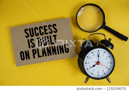 Success is Built on Planning text written on paper with magnifying glass and alarm clock on yellow background 129209078
