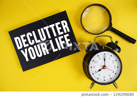 Declutter Your Life text written on paper with magnifying glass and alarm clock on yellow background Declutter Your Life text written on paper with magnifying glass and alarm clock on yellow background 129209080